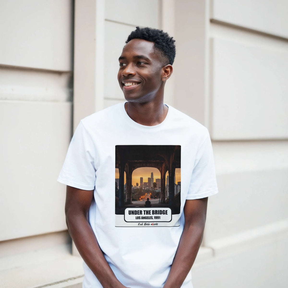Ragazzo sorridente davanti a un muro chiaro a blocchi indossa la t-shirt bianca con la stampa Rock Art «Under the Bridge – Los Angeles, 1991»