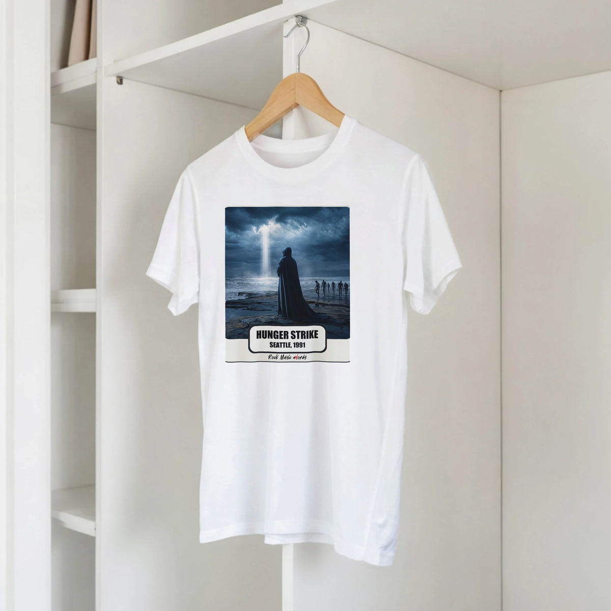 T-shirt bianca con la stampa Rock Art «Hunger Strike – Seattle, 1991» su una gruccia di legno, appesa a una libreria bianca