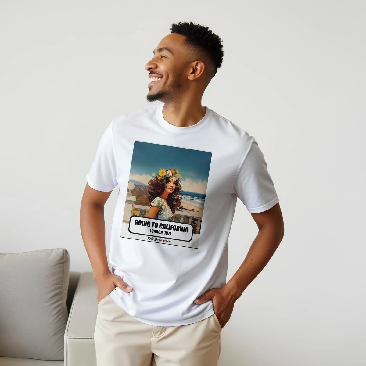 Uomo sorridente con le mani sui fianchi, accanto a un divano, indossa la t-shirt bianca con la stampa Rock Art «Going to California – London, 1971»