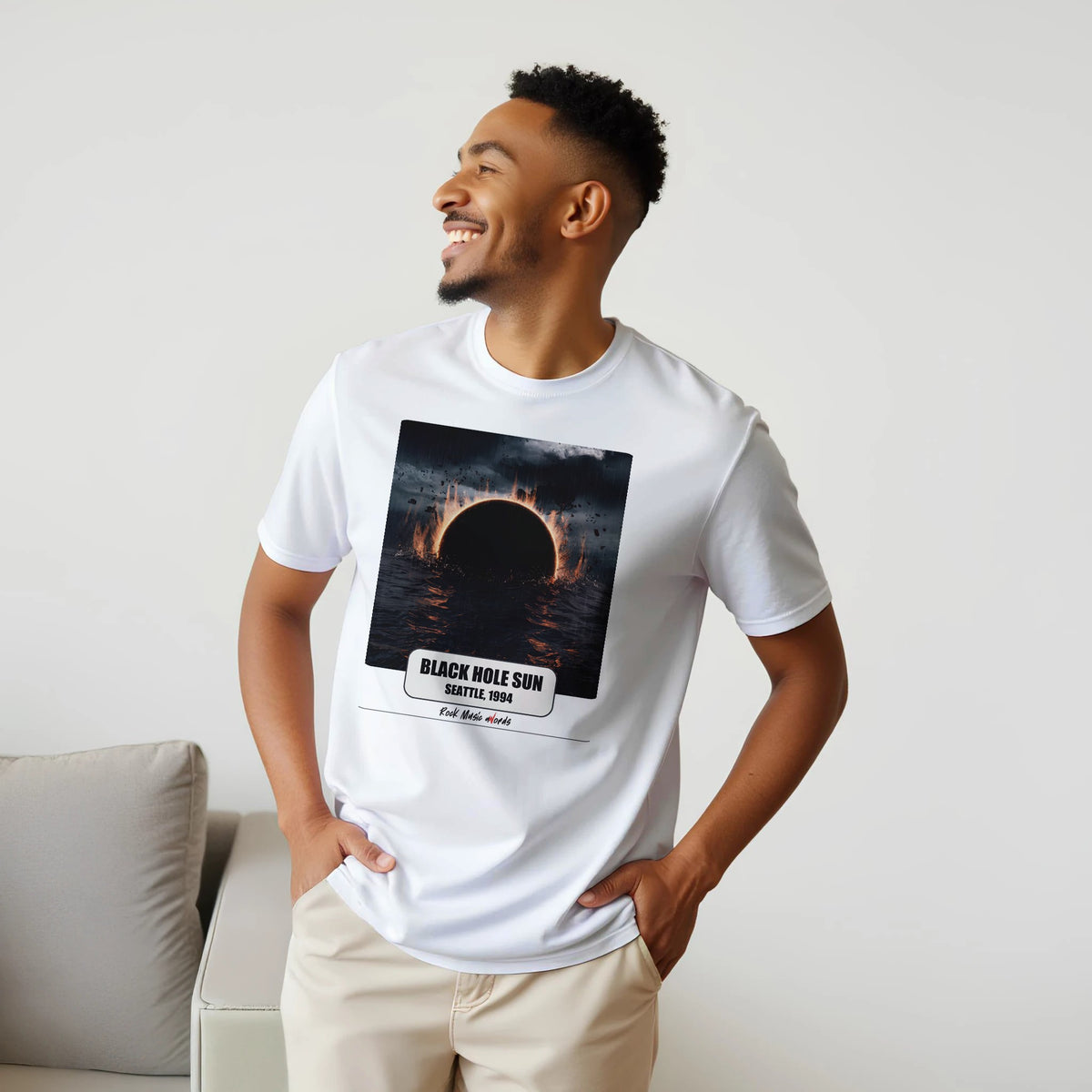 Uomo sorridente con le mani sui fianchi, accanto a un divano, indossa la t-shirt bianca con la stampa Rock Art «Black Hole Sun – Seattle, 1994»