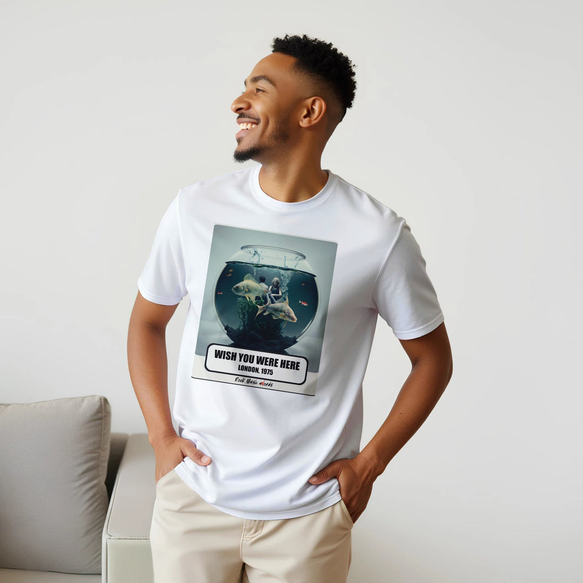 Uomo sorridente con le mani sui fianchi, accanto a un divano, indossa la t-shirt bianca con la stampa Rock Art «Wish You Were Here – London, 1975»