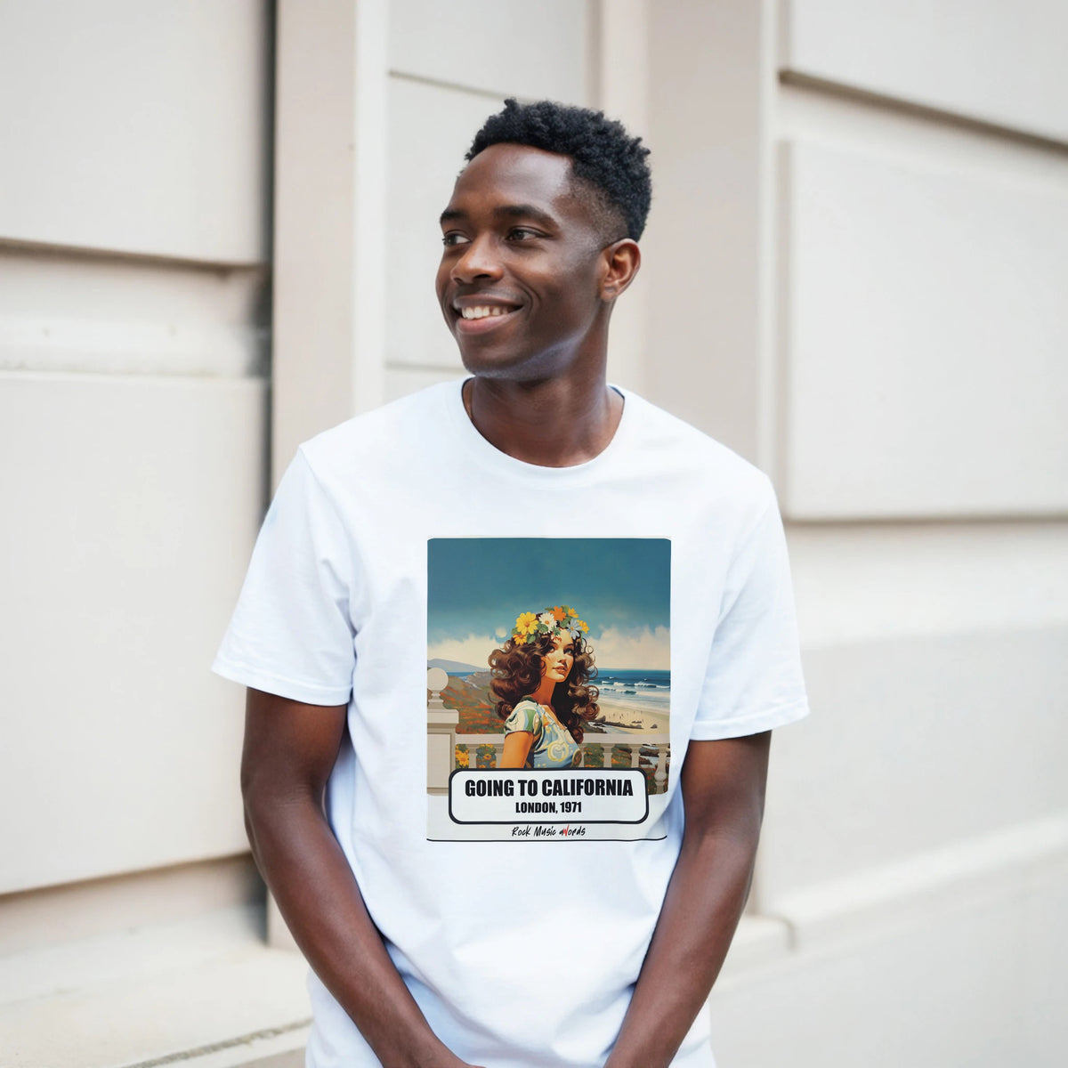 Ragazzo sorridente davanti a un muro chiaro a blocchi indossa la t-shirt bianca con la stampa Rock Art «Going to California – London, 1971»