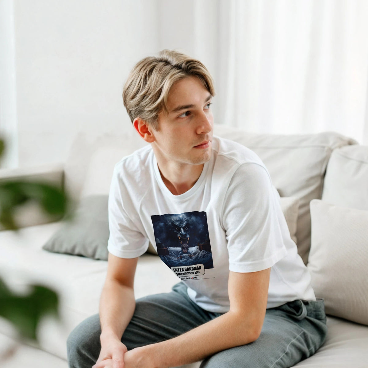 Ragazzo biondo seduto su un divano bianco, piegato in avanti, indossa la t-shirt bianca con la stampa Rock Art «Enter Sandman – San Francisco, 1991»