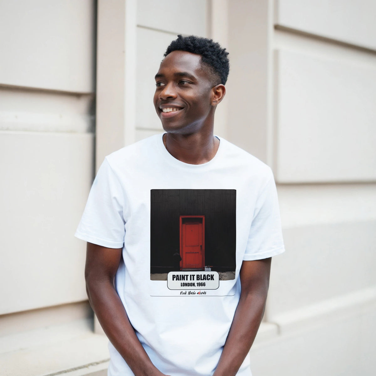 Ragazzo sorridente davanti a un muro chiaro a blocchi indossa la t-shirt bianca con la stampa Rock Art «Paint It Black – London, 1966»