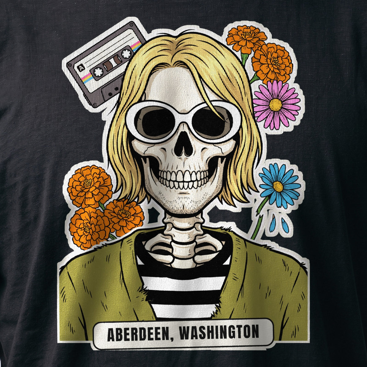 La stampa da vicino sulla t-shirt nera: la calavera Aberdeen con la cassetta, i fiori e la targhetta «Aberdeen, Washington», sul cotone (ricostruzione al computer)