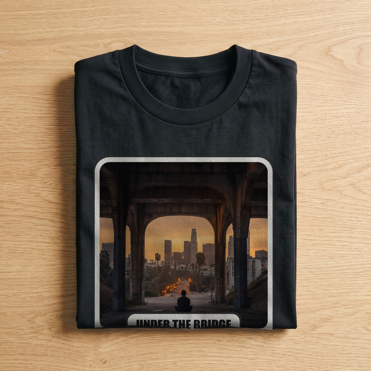 La t-shirt nera «Under the Bridge – Los Angeles, 1991» piegata su un piano di legno, come arriva a casa (ricostruzione al computer)