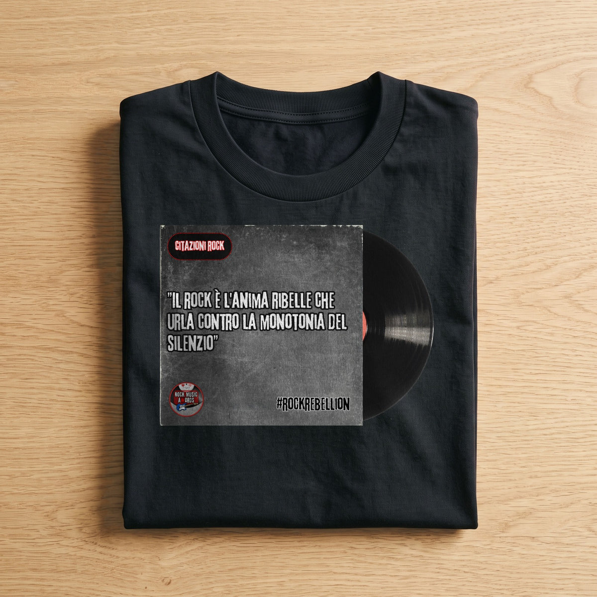 La t-shirt nera «#RockRebellion: il rock è l'anima ribelle che urla contro la monotonia del silenzio» piegata su un piano di legno, come arriva a casa (ricostruzione al computer)